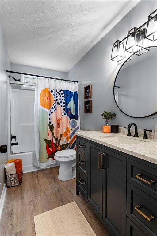 full bathroom with hardwood / wood-style flooring, vanity, toilet, shower / bath combo, and a textured ceiling