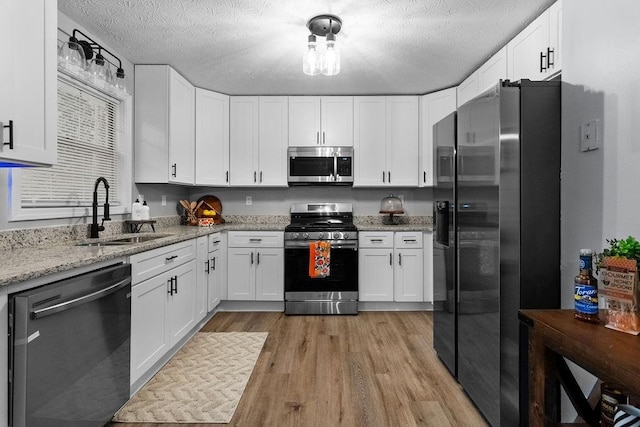 kitchen with stainless steel appliances, sink, white cabinets, and light stone counters