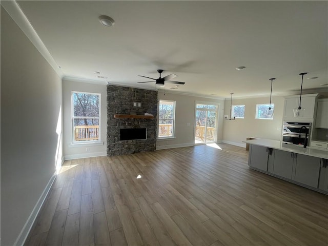 unfurnished living room featuring crown molding, a stone fireplace, light hardwood / wood-style floors, and ceiling fan