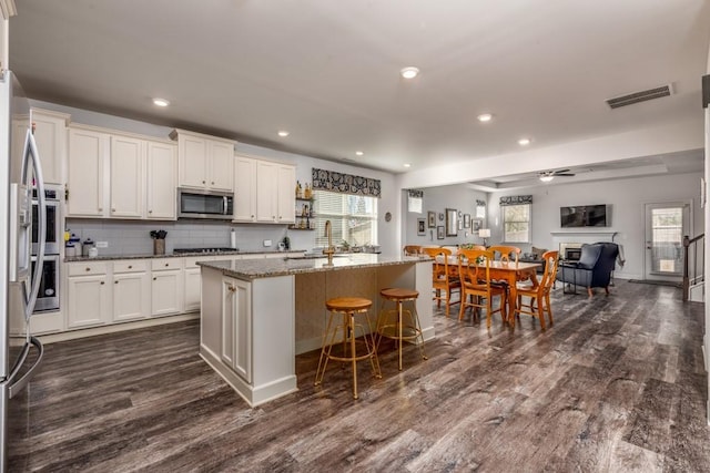 kitchen featuring tasteful backsplash, visible vents, stainless steel microwave, dark wood-type flooring, and white cabinetry