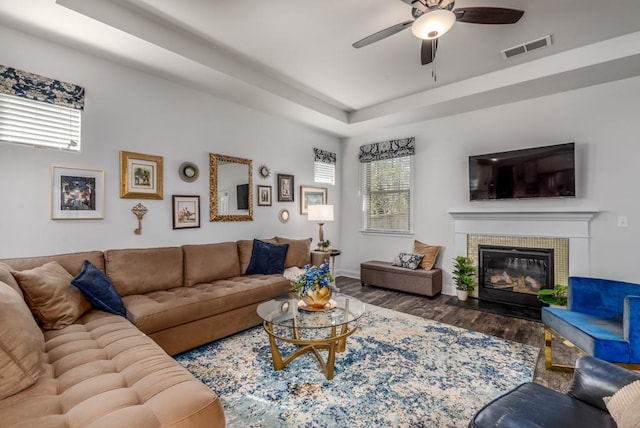 living area with ceiling fan, a fireplace, wood finished floors, visible vents, and a tray ceiling