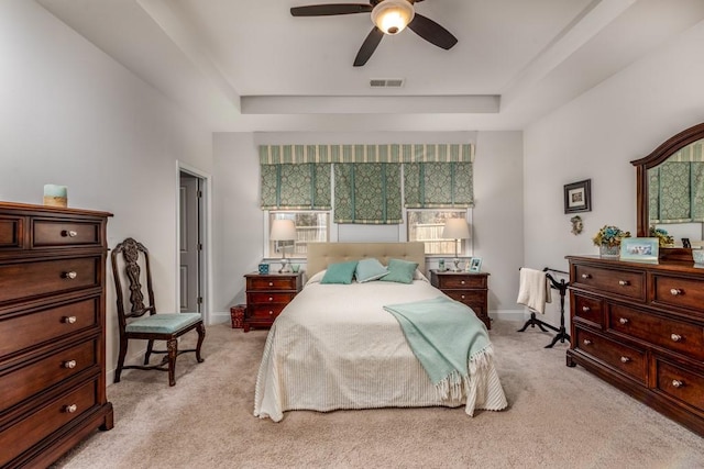 bedroom with light colored carpet, a raised ceiling, visible vents, and baseboards