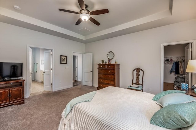 carpeted bedroom with a tray ceiling, a walk in closet, a closet, ensuite bathroom, and baseboards