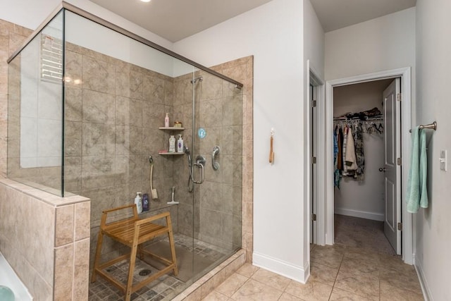 bathroom with a shower stall, a spacious closet, baseboards, and tile patterned flooring