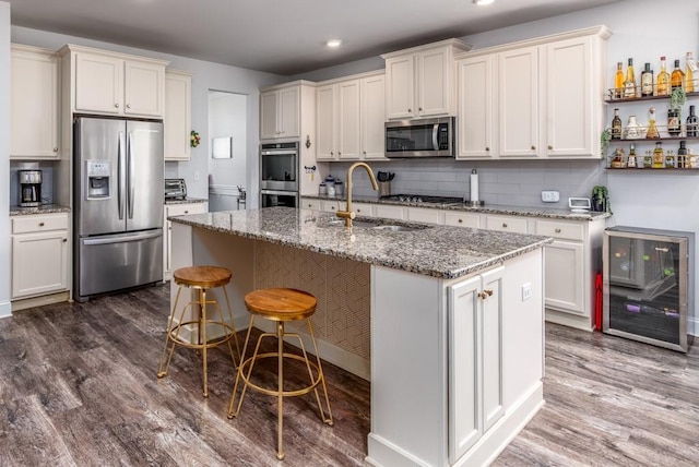 kitchen featuring dark wood finished floors, stainless steel appliances, backsplash, a kitchen island with sink, and a sink