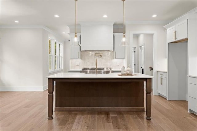 kitchen with white cabinets, hanging light fixtures, light hardwood / wood-style flooring, decorative backsplash, and an island with sink