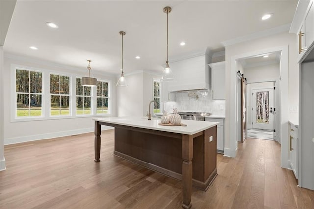 kitchen with hardwood / wood-style floors, backsplash, a center island with sink, a barn door, and decorative light fixtures