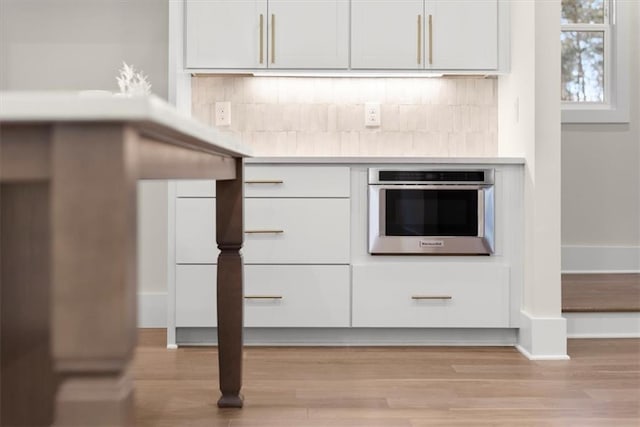 kitchen with white cabinets, decorative backsplash, stainless steel oven, and light wood-type flooring