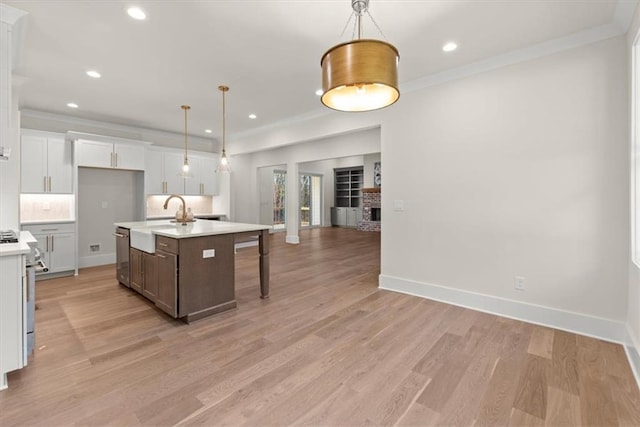 kitchen with white cabinets, pendant lighting, a center island with sink, and light hardwood / wood-style floors