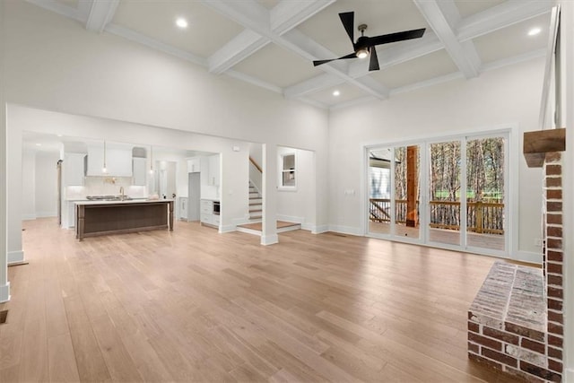 unfurnished living room featuring beam ceiling, a towering ceiling, light hardwood / wood-style floors, and ceiling fan