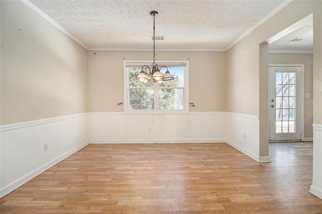 unfurnished dining area with an inviting chandelier, a textured ceiling, ornamental molding, and light wood-type flooring