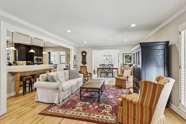 living room featuring light hardwood / wood-style floors, a healthy amount of sunlight, crown molding, and an inviting chandelier