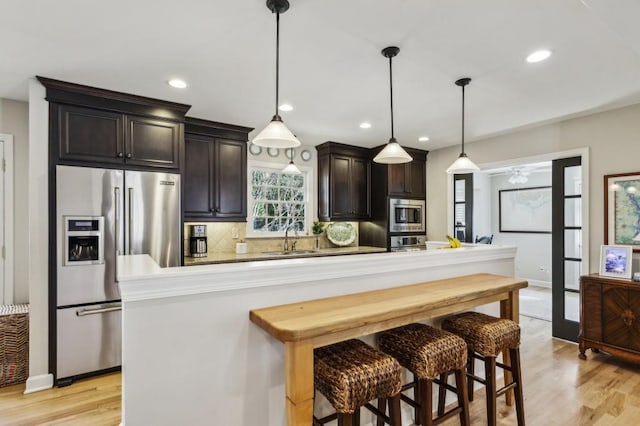 kitchen featuring pendant lighting, dark brown cabinetry, sink, and appliances with stainless steel finishes