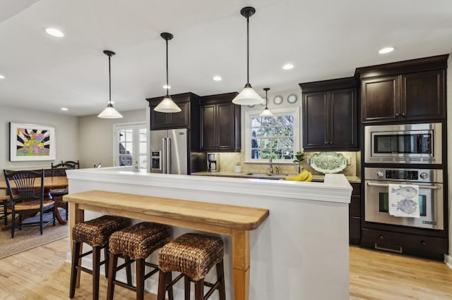 kitchen with dark brown cabinetry, a kitchen island, stainless steel appliances, and decorative light fixtures