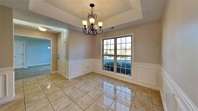 unfurnished dining area with a tray ceiling, light tile patterned floors, and a notable chandelier