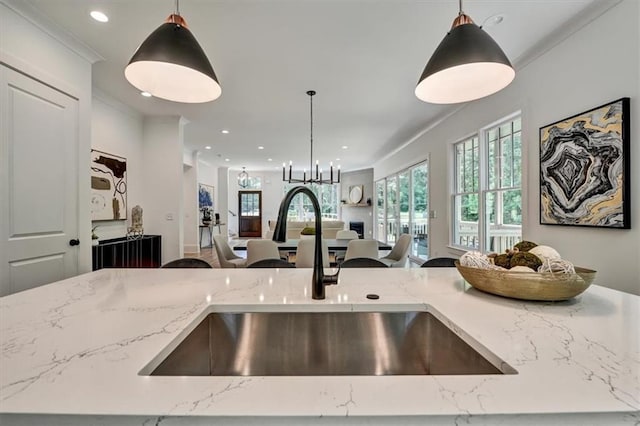 kitchen with sink, hanging light fixtures, light stone counters, crown molding, and a chandelier