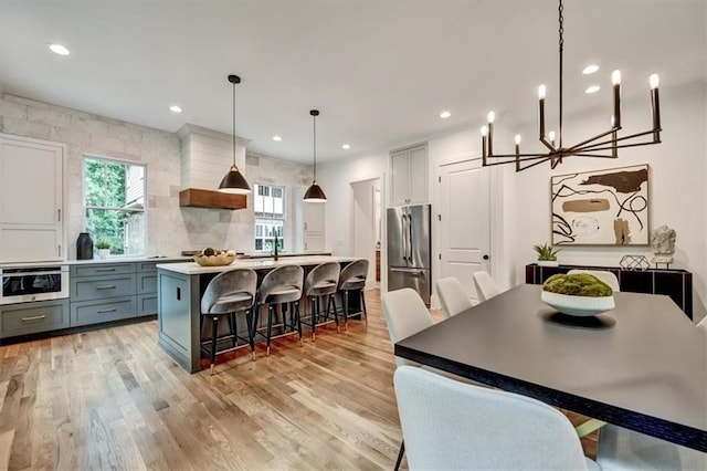 kitchen with stainless steel refrigerator, light hardwood / wood-style flooring, gray cabinetry, and decorative light fixtures