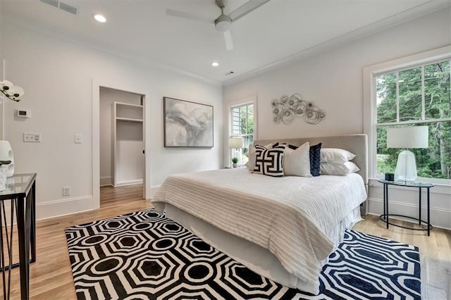 bedroom with light hardwood / wood-style floors, a spacious closet, ceiling fan, and ornamental molding