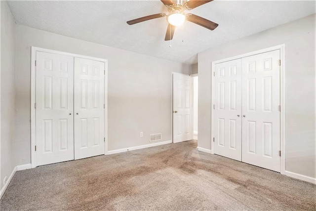 unfurnished bedroom featuring carpet flooring, two closets, and ceiling fan