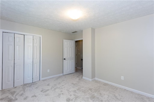 unfurnished bedroom with a textured ceiling, light carpet, and a closet