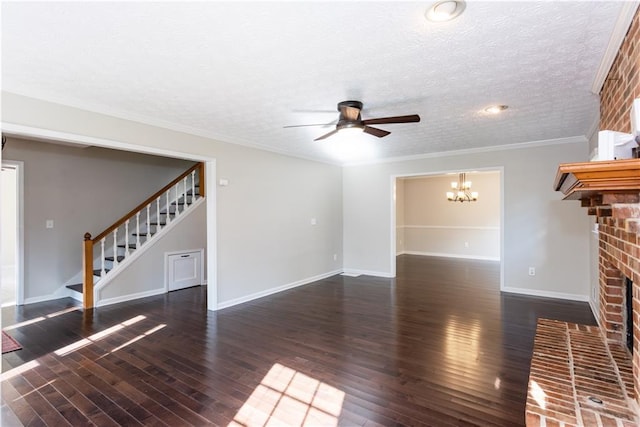 unfurnished living room featuring ornamental molding, dark wood-type flooring, a brick fireplace, and ceiling fan with notable chandelier