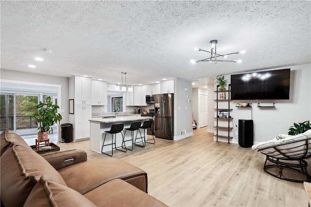 living area with light wood finished floors, baseboards, an inviting chandelier, a textured ceiling, and recessed lighting