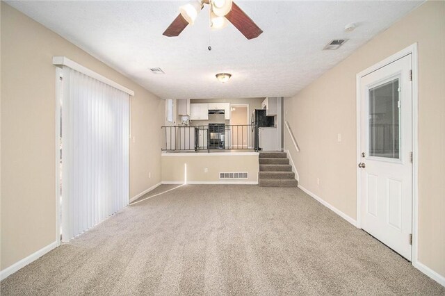 unfurnished living room featuring light carpet, a textured ceiling, and ceiling fan