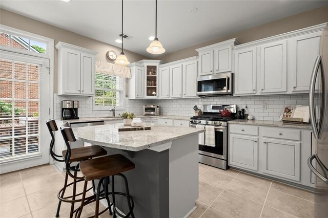 2303 Waters Edge Trl, Roswell, GA 30075 - kitchen featuring appliances with stainless steel finishes, a center island, backsplash, light tile patterned floors, and a breakfast bar
