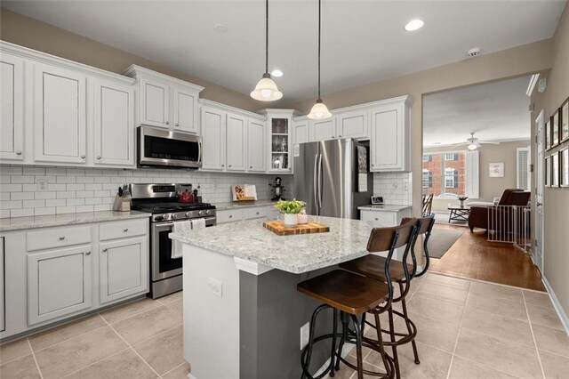 2303 Waters Edge Trl, Roswell, GA 30075 - kitchen featuring appliances with stainless steel finishes, light tile patterned floors, tasteful backsplash, a kitchen island, and glass insert cabinets