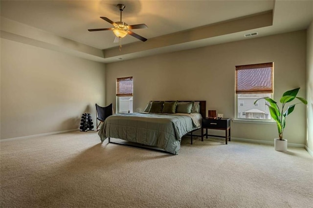 bedroom featuring ceiling fan, a tray ceiling, and multiple windows