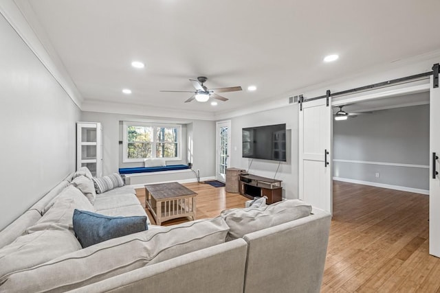 living room featuring a barn door, crown molding, hardwood / wood-style floors, and ceiling fan