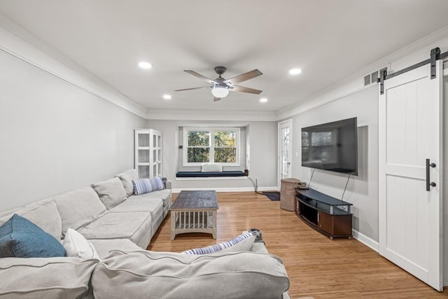 living room with light wood-type flooring, a barn door, crown molding, and ceiling fan