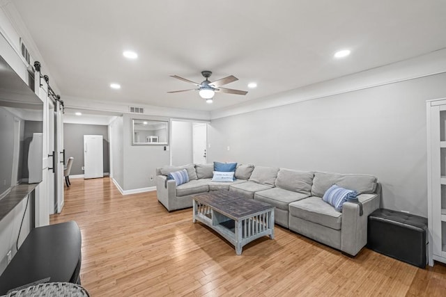 living room with a barn door, ceiling fan, and light hardwood / wood-style floors