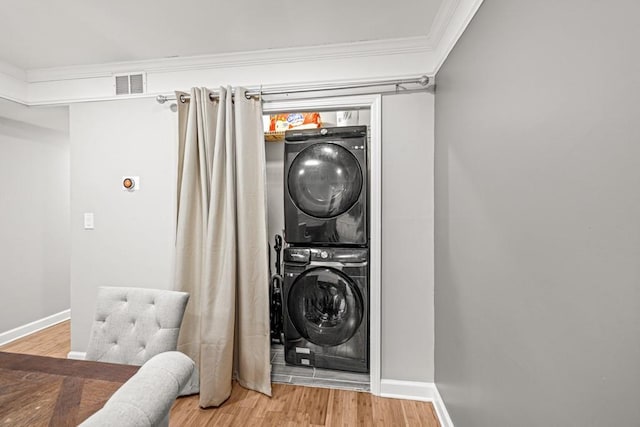 laundry area with crown molding, stacked washer and dryer, and wood-type flooring