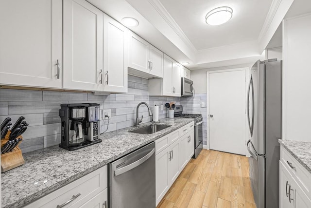 kitchen with white cabinets, crown molding, sink, appliances with stainless steel finishes, and light hardwood / wood-style floors