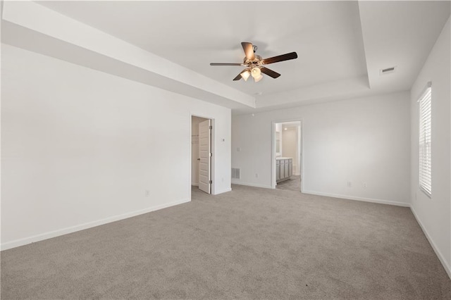 carpeted empty room with baseboards, a tray ceiling, visible vents, and a ceiling fan