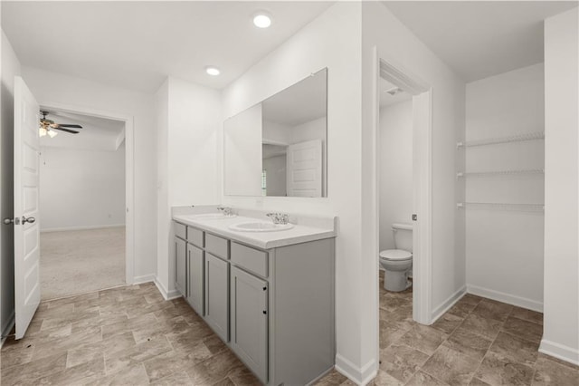 full bath with baseboards, double vanity, ceiling fan, toilet, and a sink