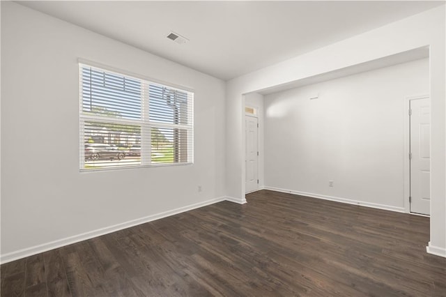 empty room with dark wood-type flooring, visible vents, and baseboards