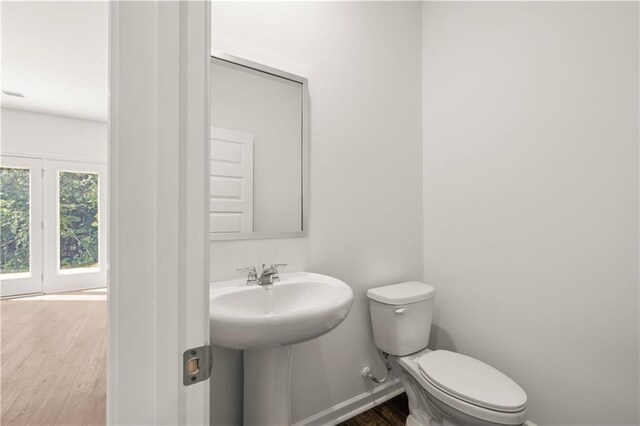 half bathroom with baseboards, toilet, a sink, and wood finished floors