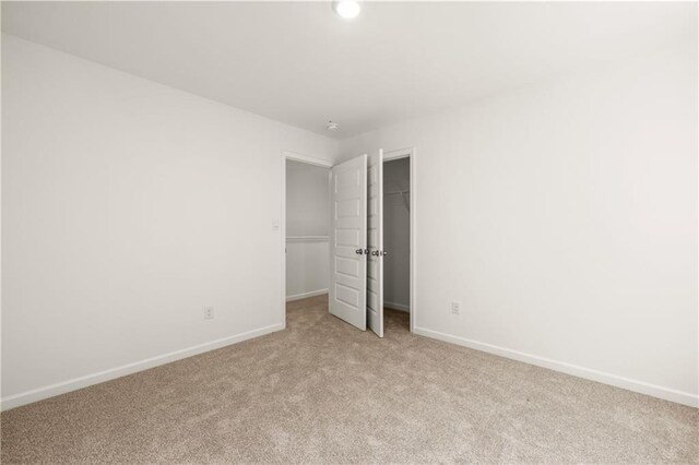 unfurnished bedroom featuring baseboards, a spacious closet, and light carpet