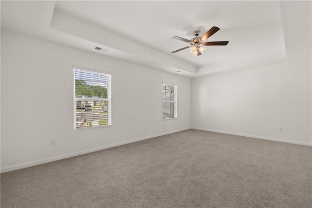 unfurnished room featuring visible vents, carpet, baseboards, a ceiling fan, and a tray ceiling