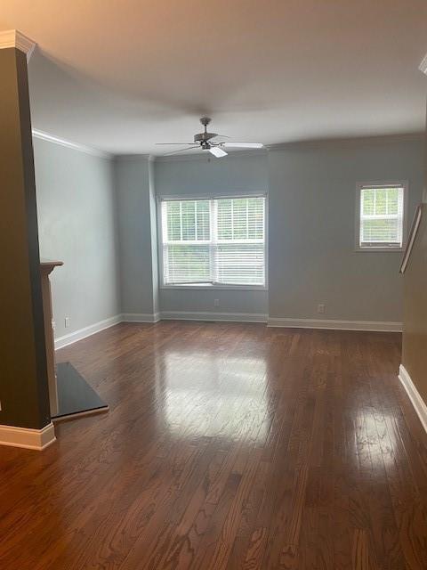 empty room with ornamental molding, dark wood finished floors, a wealth of natural light, and a ceiling fan