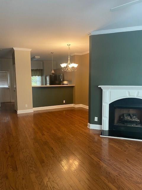 unfurnished living room with a chandelier, a fireplace with raised hearth, dark wood-style flooring, baseboards, and ornamental molding