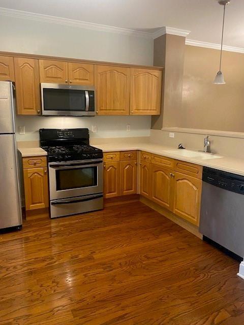 kitchen featuring stainless steel appliances, light countertops, crown molding, and dark wood-style floors