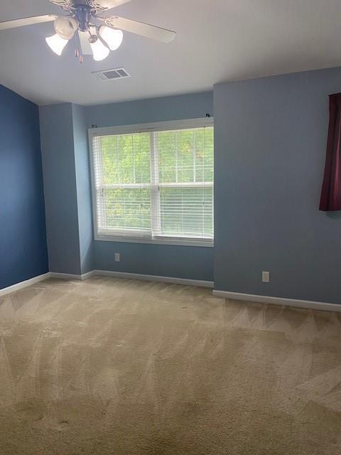 carpeted spare room featuring baseboards, visible vents, and a ceiling fan