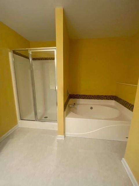 full bath featuring a shower stall, a bath, and baseboards