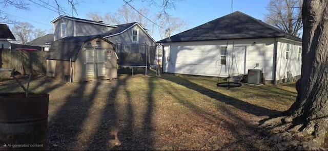 rear view of property featuring cooling unit, a yard, a trampoline, and an outbuilding