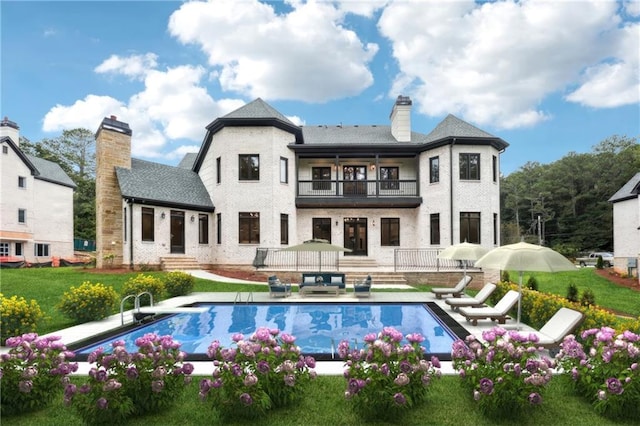 back of property with a patio, a chimney, entry steps, a balcony, and an outdoor pool