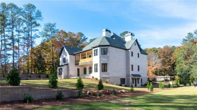 back of property with a lawn, a chimney, and a balcony