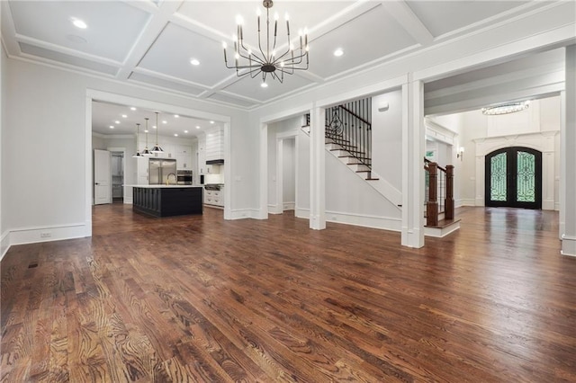 unfurnished living room featuring french doors, dark wood finished floors, stairway, an inviting chandelier, and coffered ceiling